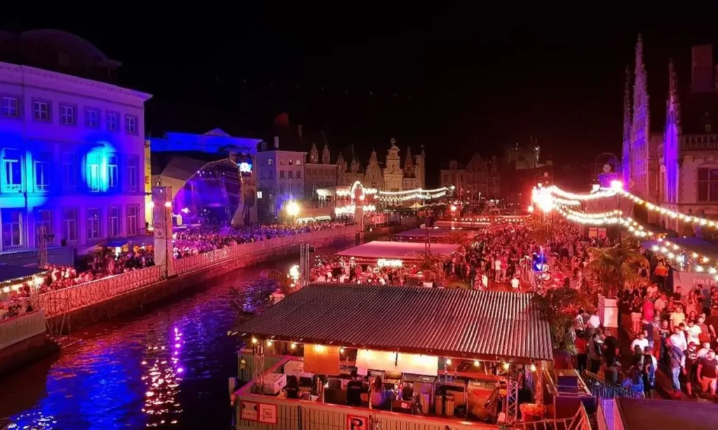 Ghent Light Festival at night with colorful lights, crowds, and reflections on the water.