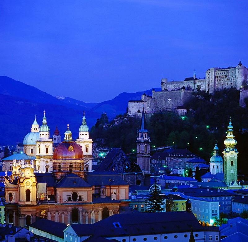 View of Salzburg, Austria, with illuminated historic buildings against the clear sky.