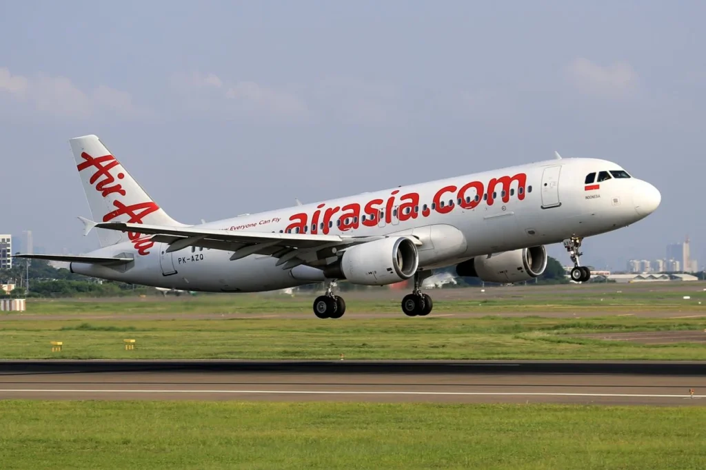 An AirAsia Airbus A320 airplane with its landing gear extended touching down on an airport runway