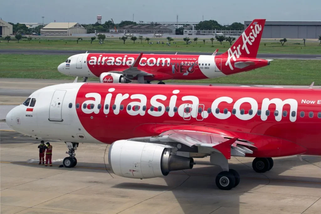Two red and white AirAsia passenger airplanes parked on an airport tarmac