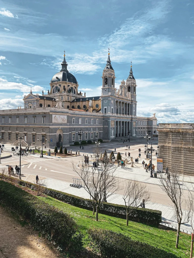 Almudena Cathedral in Madrid showing its grand stone facade, twin spires, and central dome under a blue sky