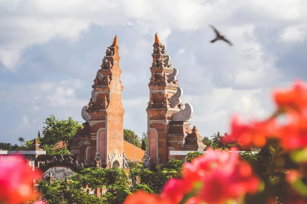 A stone split gate in Bali framed by red flowers