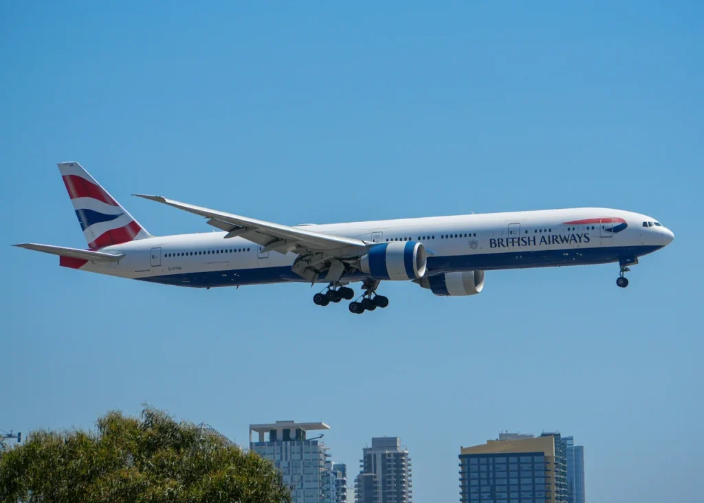 British Airways Boeing 777-300ER widebody jet descending over a city skyline with landing gear deployed