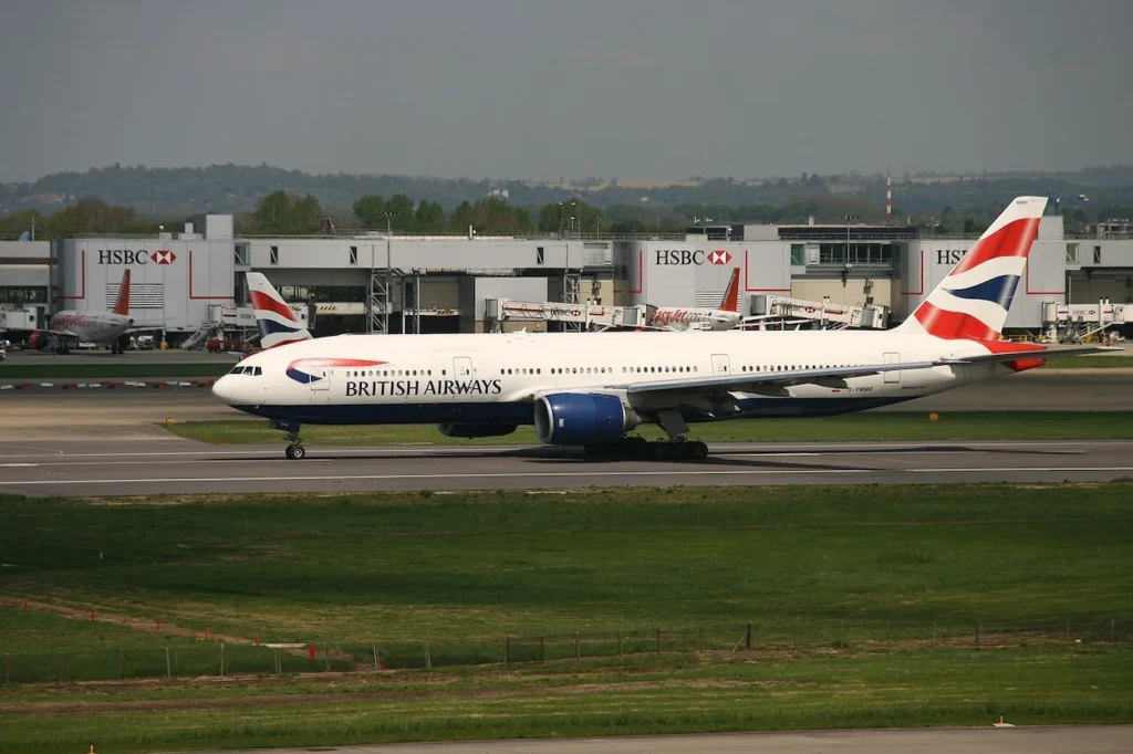 A British Airways Boeing 777 passenger aircraft taxiing on the tarmac in front of airport terminal gates