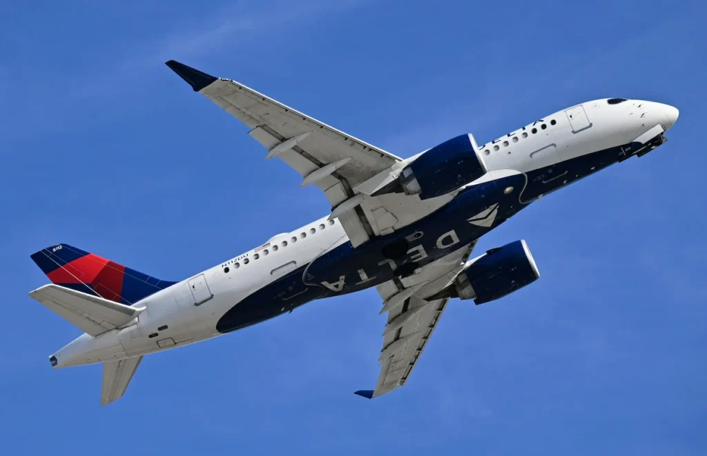 Delta Air Lines Airbus A220 commercial passenger airplane banking upward into a clear blue sky during takeoff