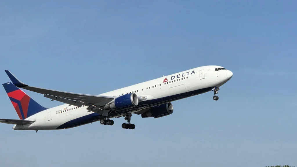 Delta Air Lines Boeing 767 jetliner climbing into a light blue sky with landing gear down