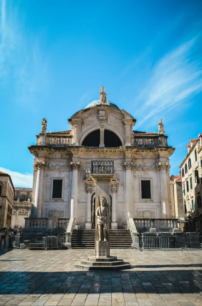 Orlando's Column standing in front of Saint Blaise Church facade under a blue sky in Dubrovnik