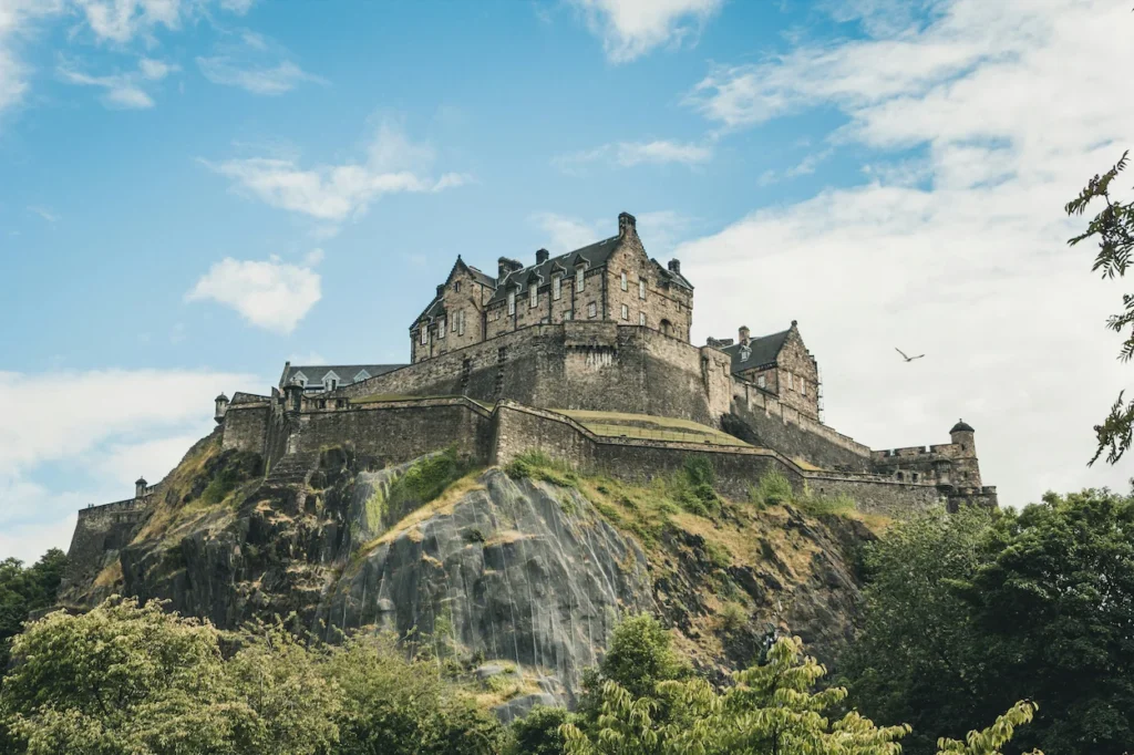 Edinburgh Castle standing on top of a steep rocky cliff against a cloudy blue sky