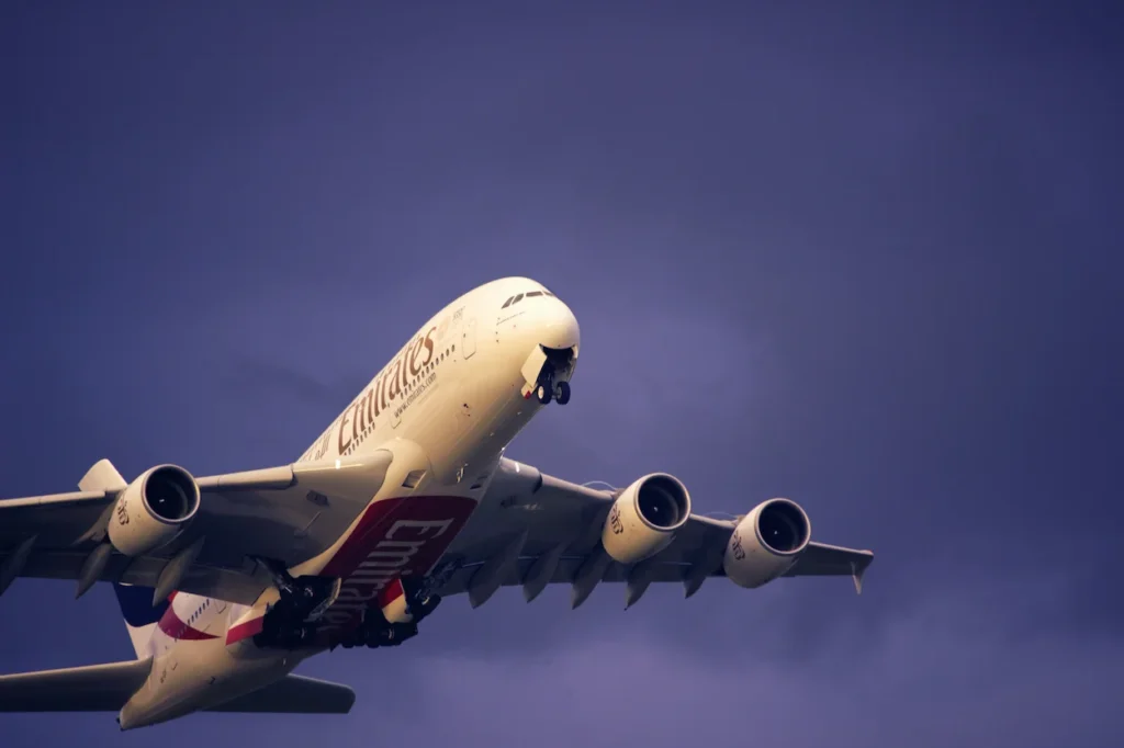 Emirates Airbus A380 double-decker passenger airplane climbing steeply into a dark purple sky after takeoff
