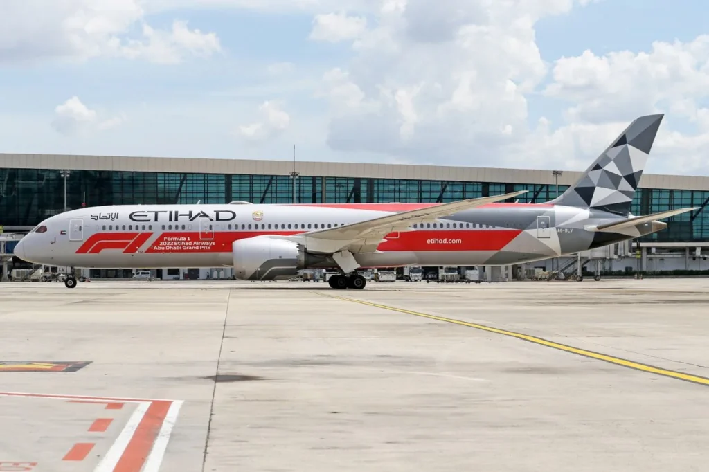 An Etihad Airways Boeing 787-9 Dreamliner in a Formula 1 Abu Dhabi Grand Prix livery parked at an airport terminal.