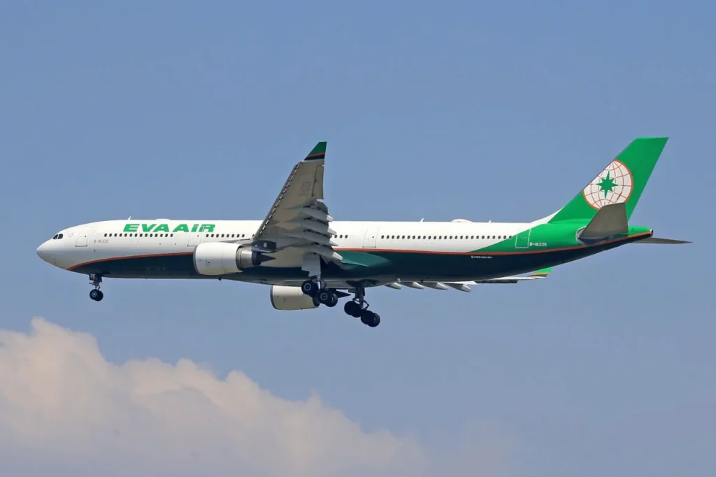 A green and white EVA Air Airbus A330 passenger plane flying with landing gear down