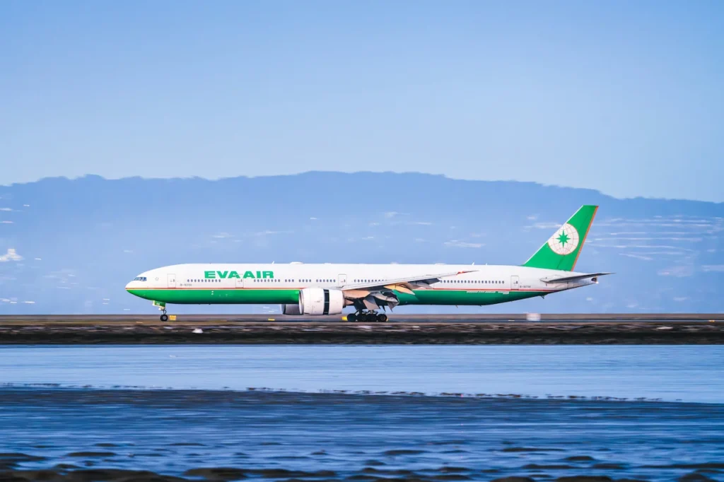 EVA Air Boeing 777 passenger aircraft taxiing on a coastal runway next to blue water
