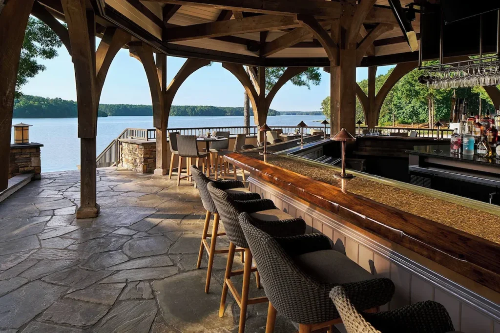 Covered lakeside bar with woven barstools, stone floors, and expansive lake views