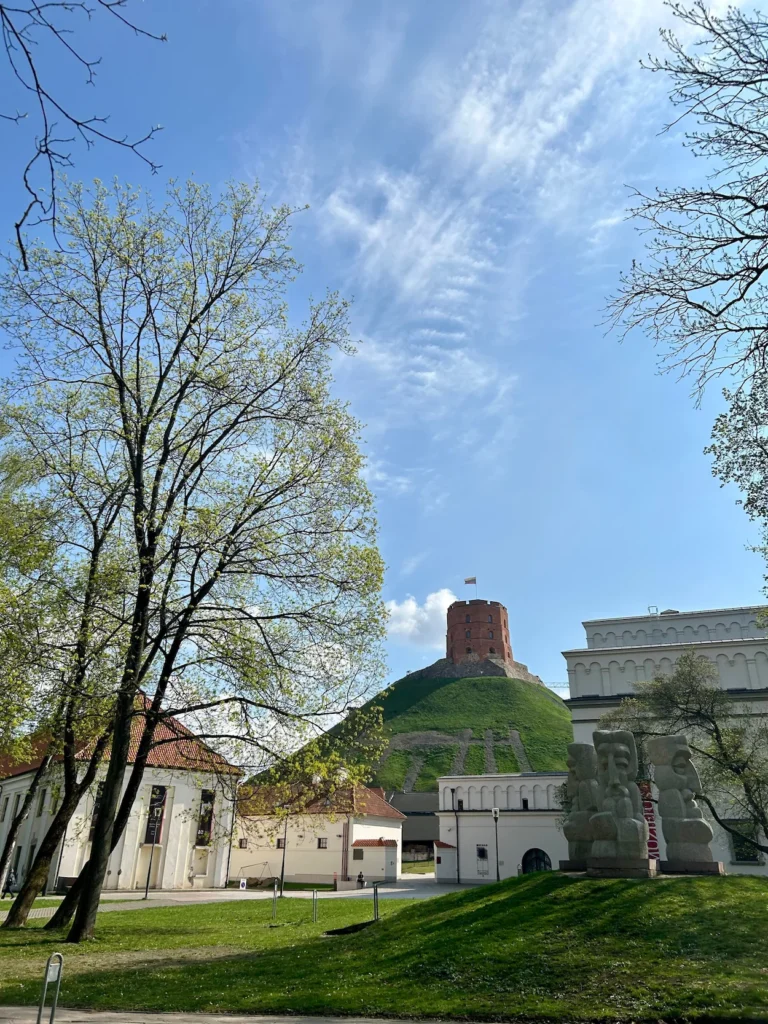 Gediminas' Tower on a green hill behind trees and historic buildings under a blue sky in Vilnius