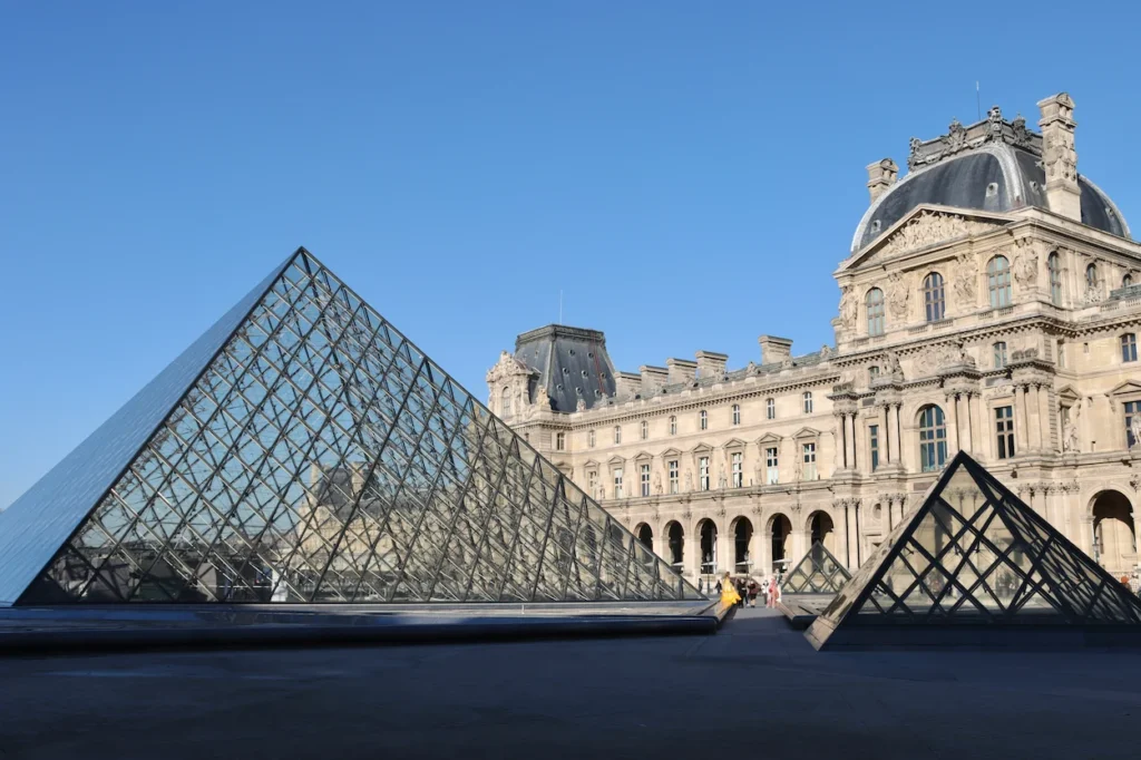Louvre Pyramid and historic palace building under a bright blue sky in Paris