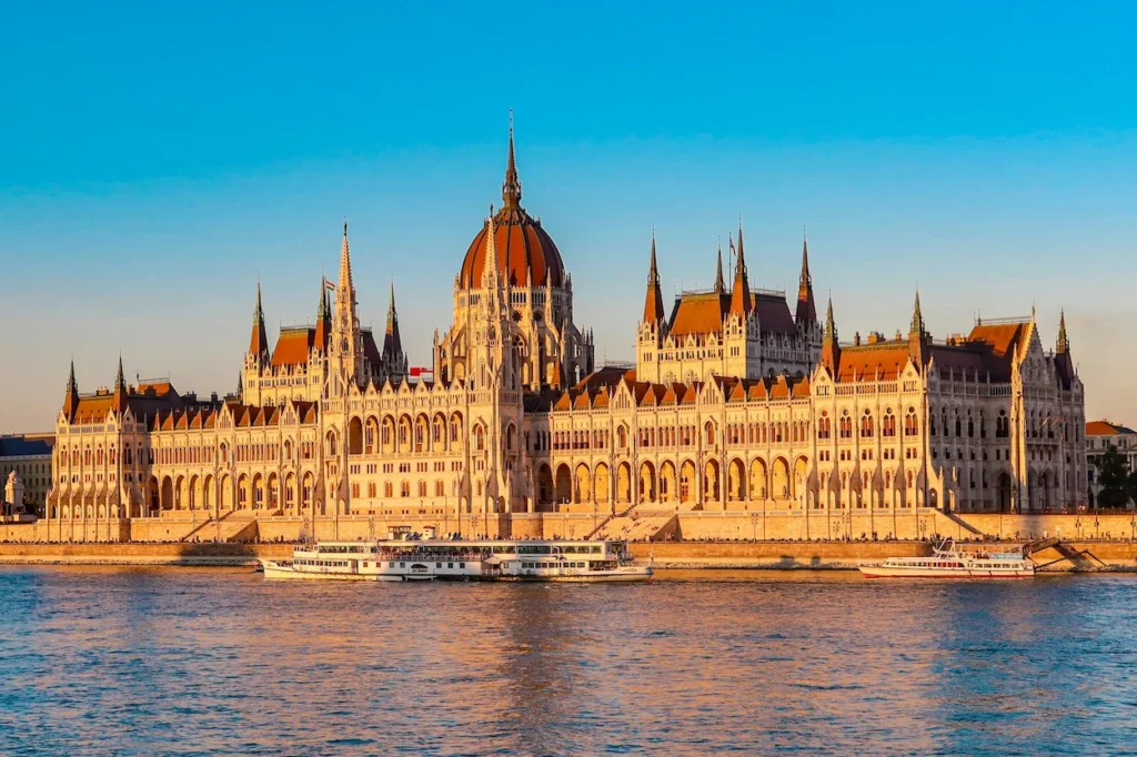 Hungarian Parliament Building in Budapest illuminated by sunlight along the Danube River bank under a clear blue sky