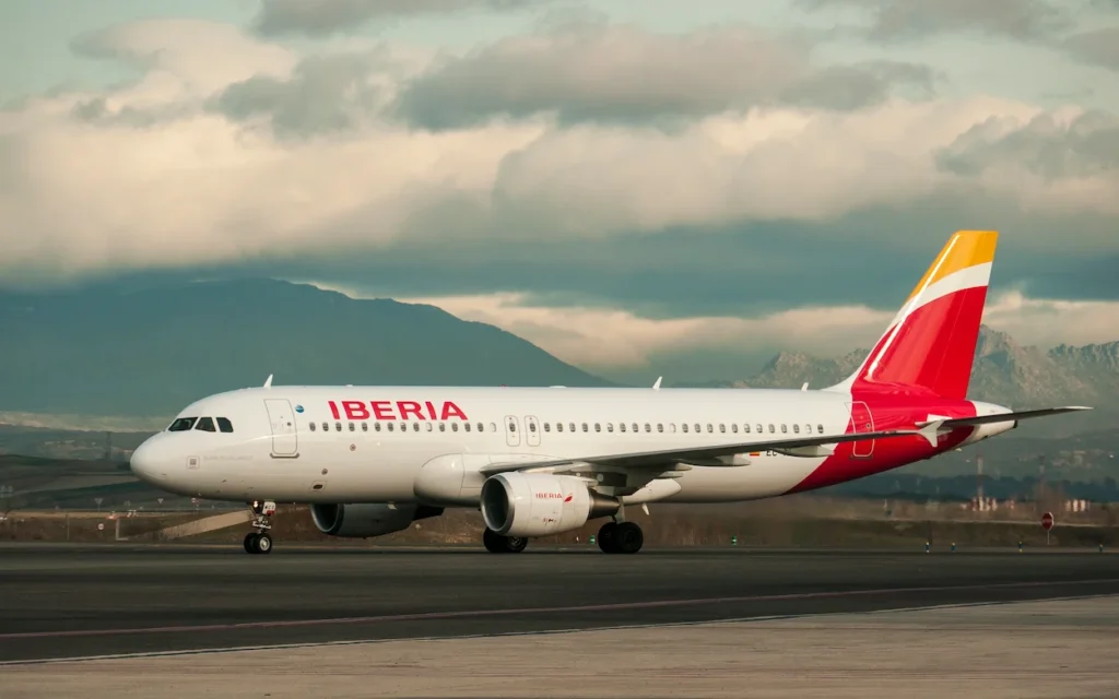 An Iberia Airbus A320 commercial airplane taxiing on an airport runway under a cloudy sky