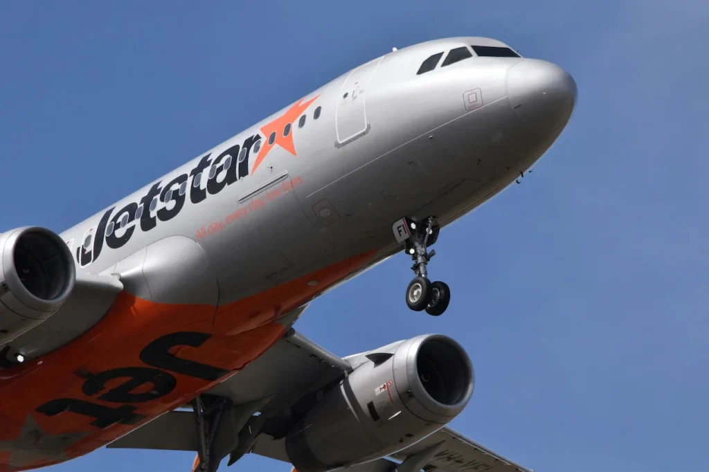 A close-up, low-angle shot of a silver and orange Jetstar Airways Airbus A320 airplane