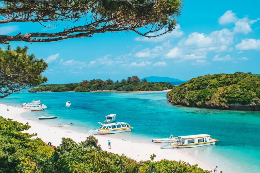 Glass-bottom boats anchored on a white sand beach at Kabira Bay under a blue sky
