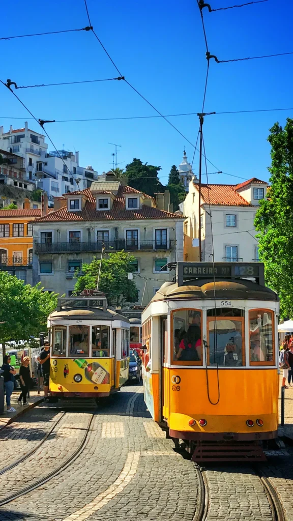 Yellow Tram 28 vehicles passing each other on cobblestone tracks in Lisbon with historic hillside houses behind