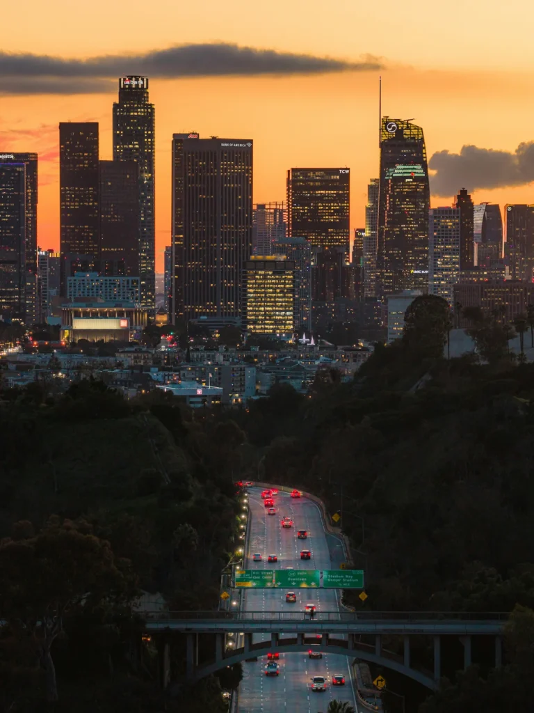 Downtown Los Angeles skyline and winding highway traffic at golden hour sunset