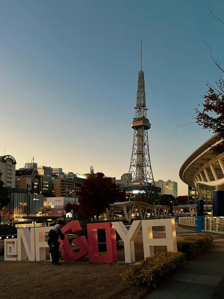 A large Nagoya sign on a lawn with the Chubu Electric Power MIRAI TOWER in the background