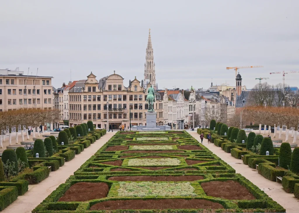 Manicured hedges of Mont des Arts garden looking toward a historic spire in Brussels