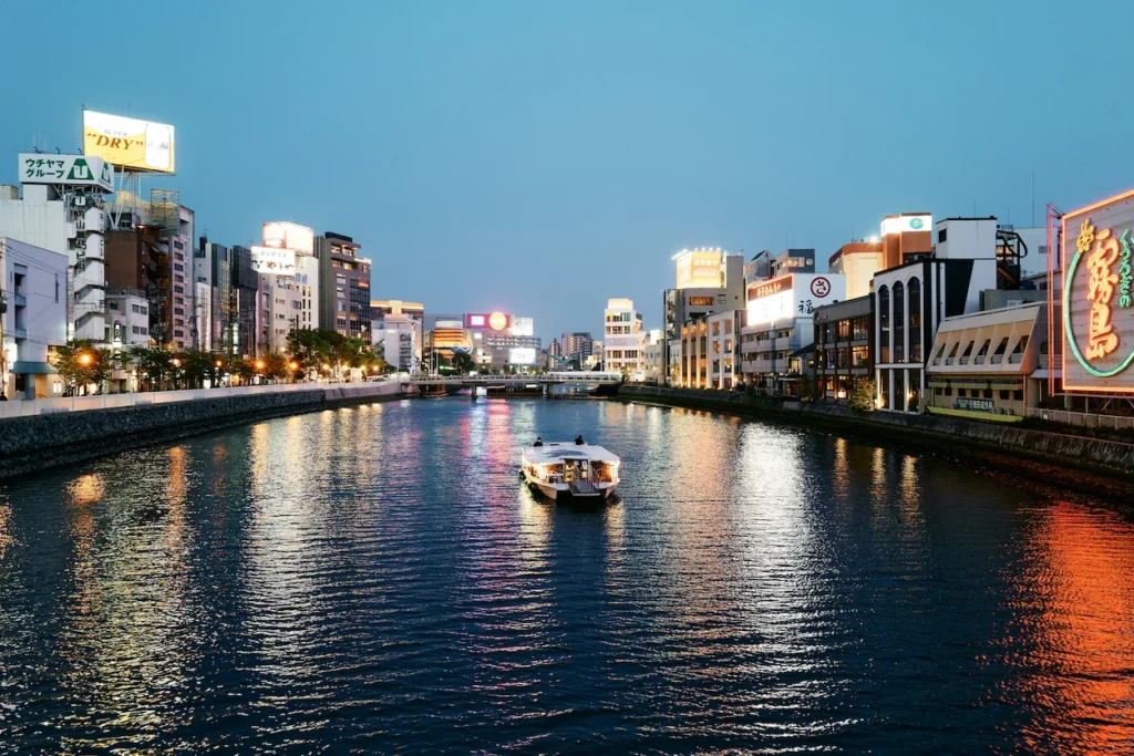 A river cruise boat cruising past illuminated city buildings at dusk