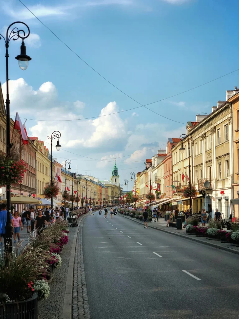 Pedestrians walking down the historic Nowy Świat Street in Warsaw under a blue sky