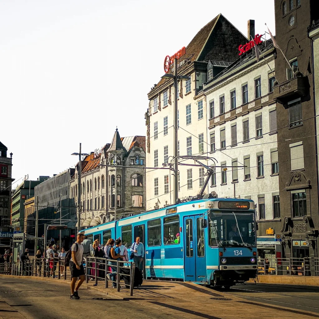 A blue city tram stopping next to a platform in historic downtown Oslo