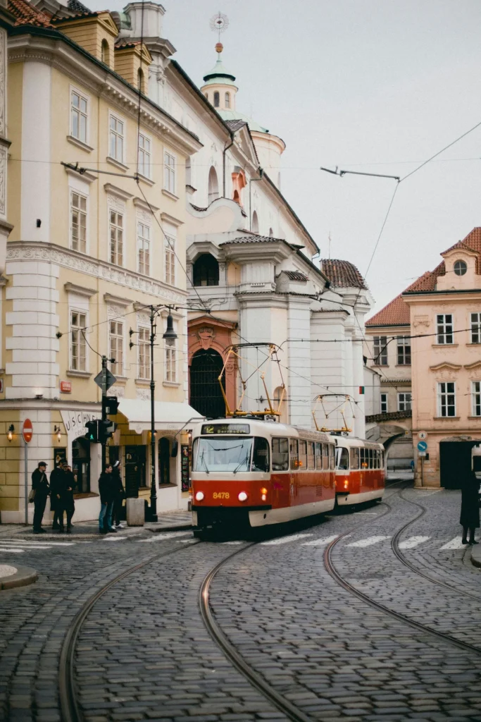 A red and white historic tram navigating a cobblestone curve past baroque buildings in Prague