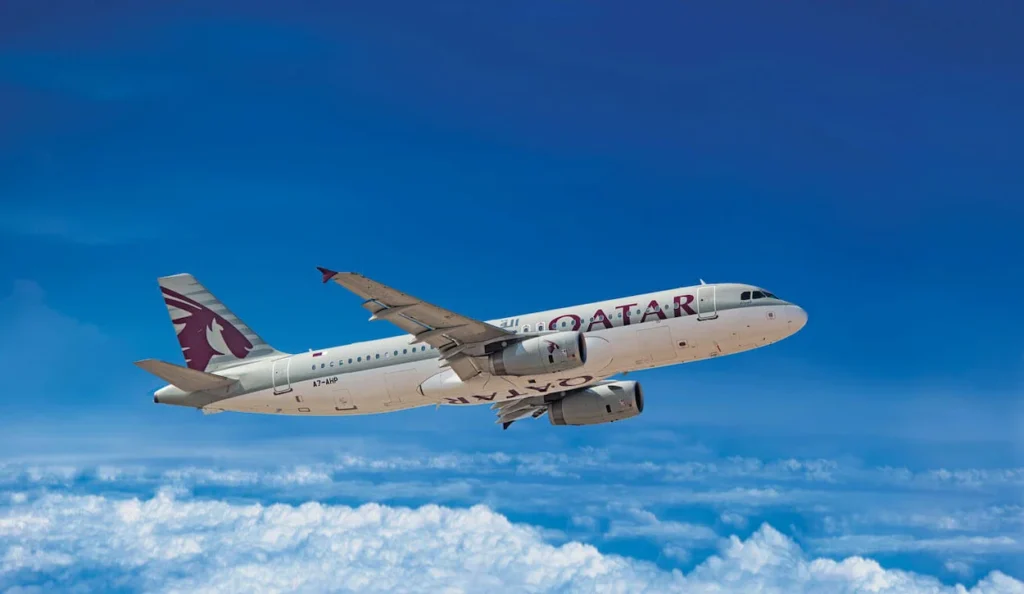 A Qatar Airways Airbus A320 flying high in a bright blue sky above white clouds