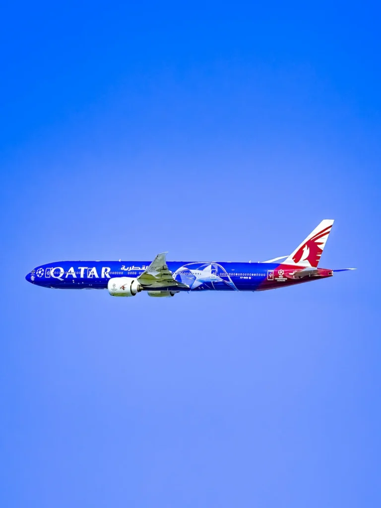 Qatar Airways Boeing 777 in blue UEFA Champions League livery flying through a clear blue sky
