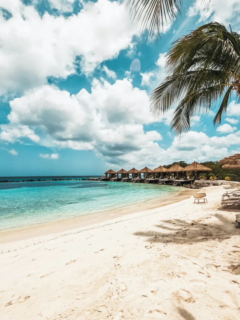 Thatch-roof beach cabanas on Renaissance Island in Aruba with turquoise water and palm trees