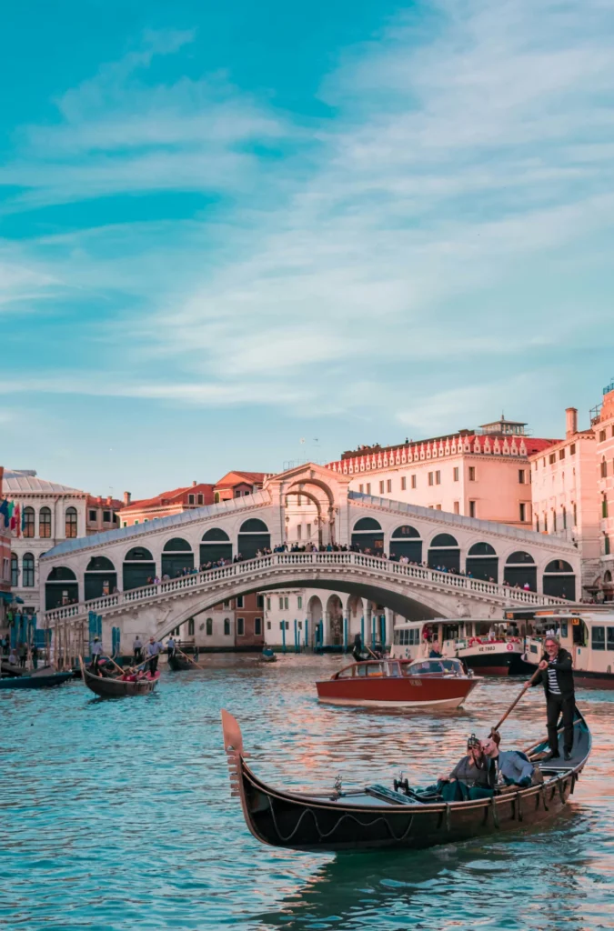 Gondola with passengers navigating the Grand Canal near Rialto Bridge under blue sky