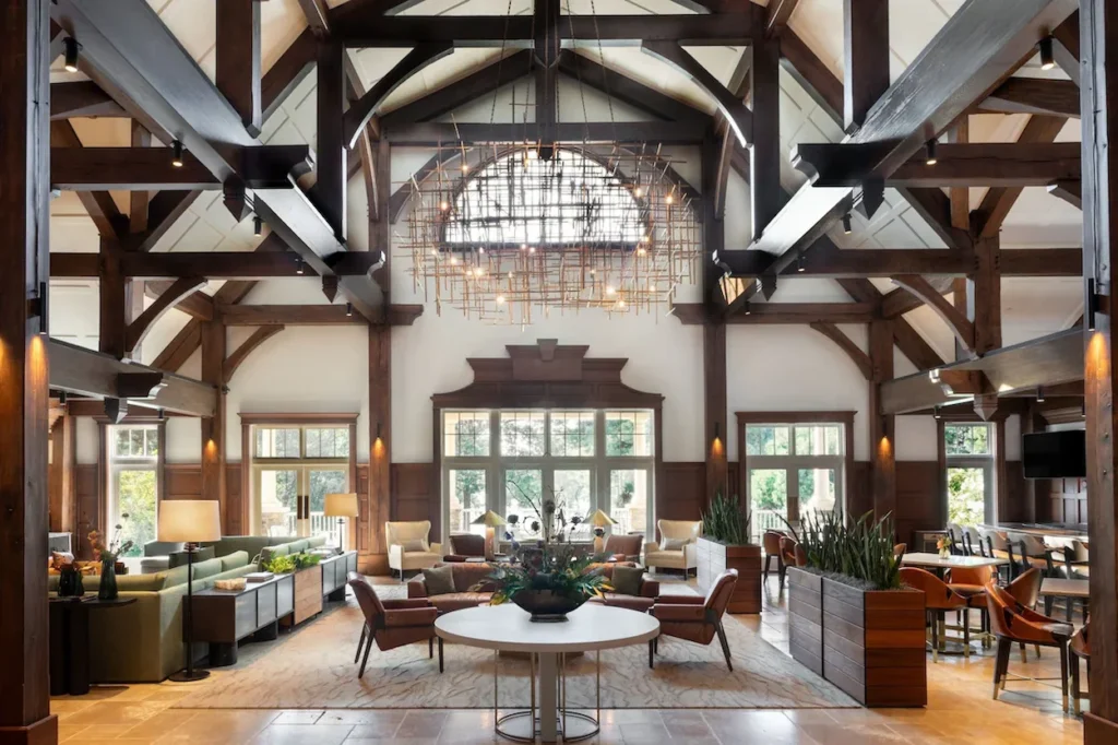 Luxury resort lobby with dark wood ceiling beams, plush armchairs, and a large central chandelier