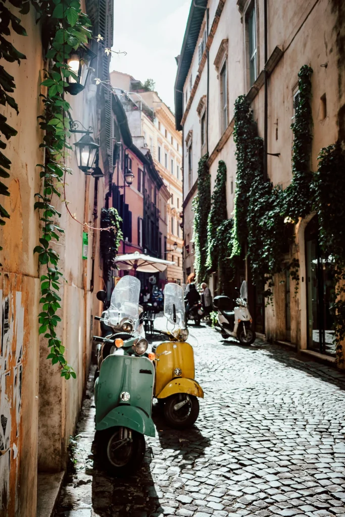 Vintage green and yellow scooters parked on a narrow cobblestone street in Rome