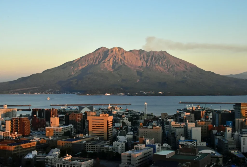 Sakurajima volcano emitting smoke across a bay from a city skyline