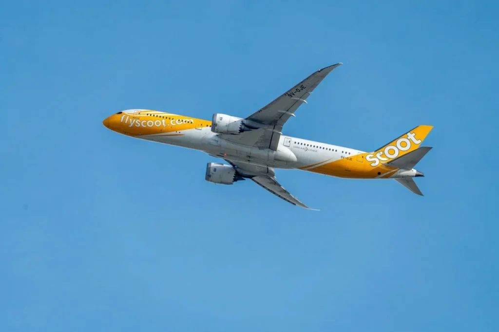 An under-belly view of a yellow and white Scoot Boeing 787 Dreamliner passenger airplane