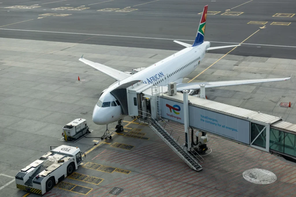 South African Airways Airbus A320 parked at a terminal gate connected to a jet bridge