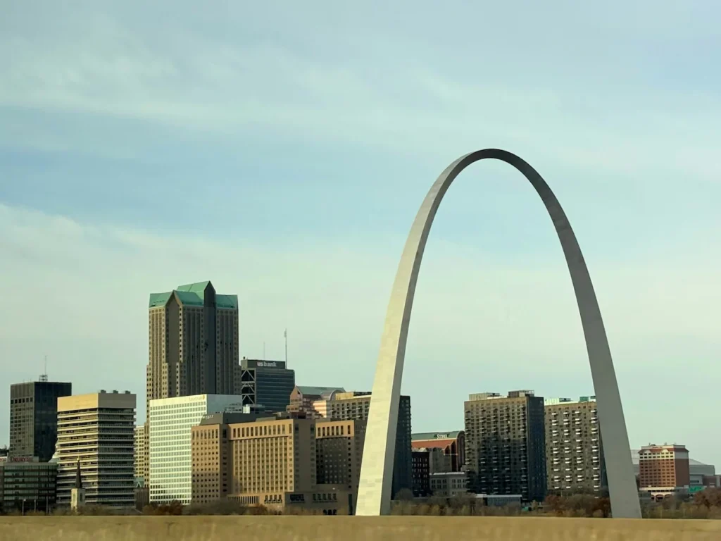 The stainless steel Gateway Arch framing the downtown St. Louis skyline under a pale blue sky