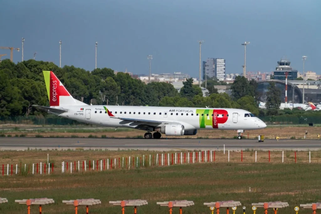 A white TAP Express Embraer E190 regional jet with a red and green tail taxiing on an airport runway