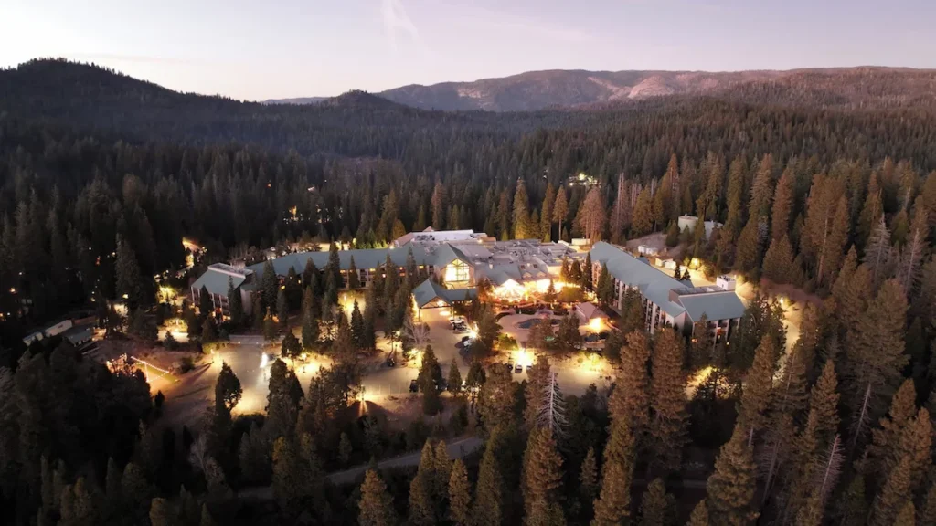 Aerial dusk view of Tenaya Lodge resort illuminated among dense pine trees and mountains