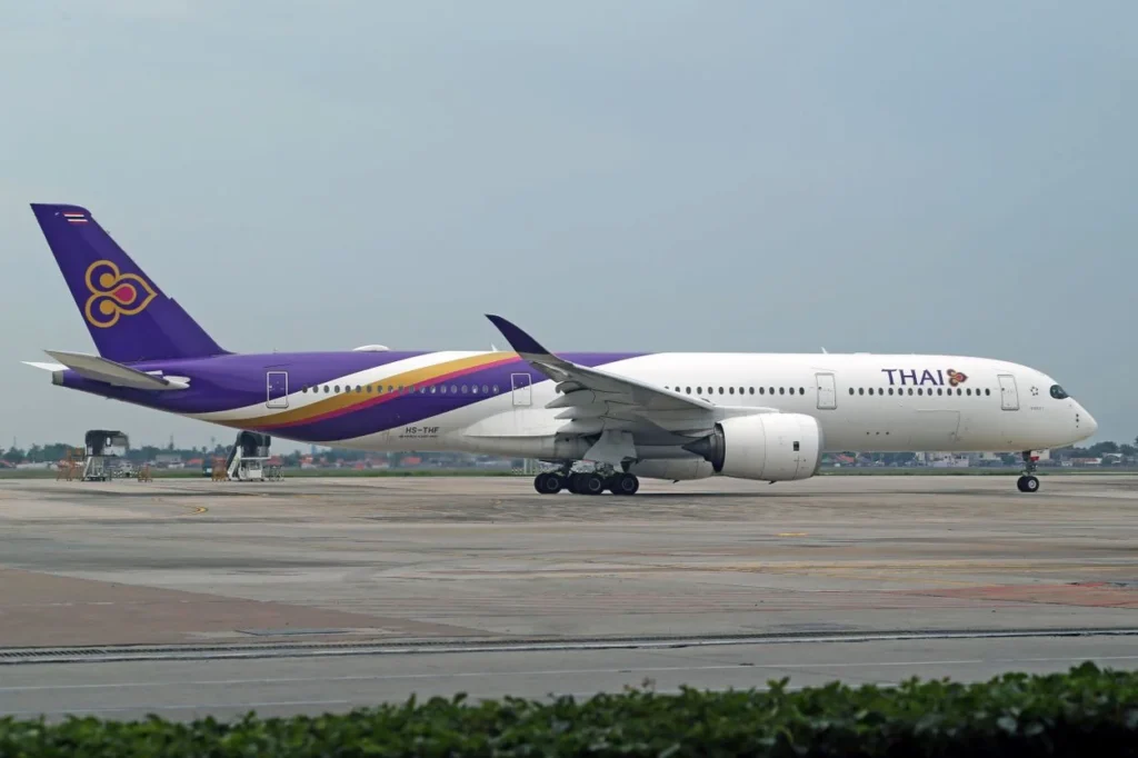 A white and purple Thai Airways Airbus A350-900 airplane taxiing slowly on an airport tarmac