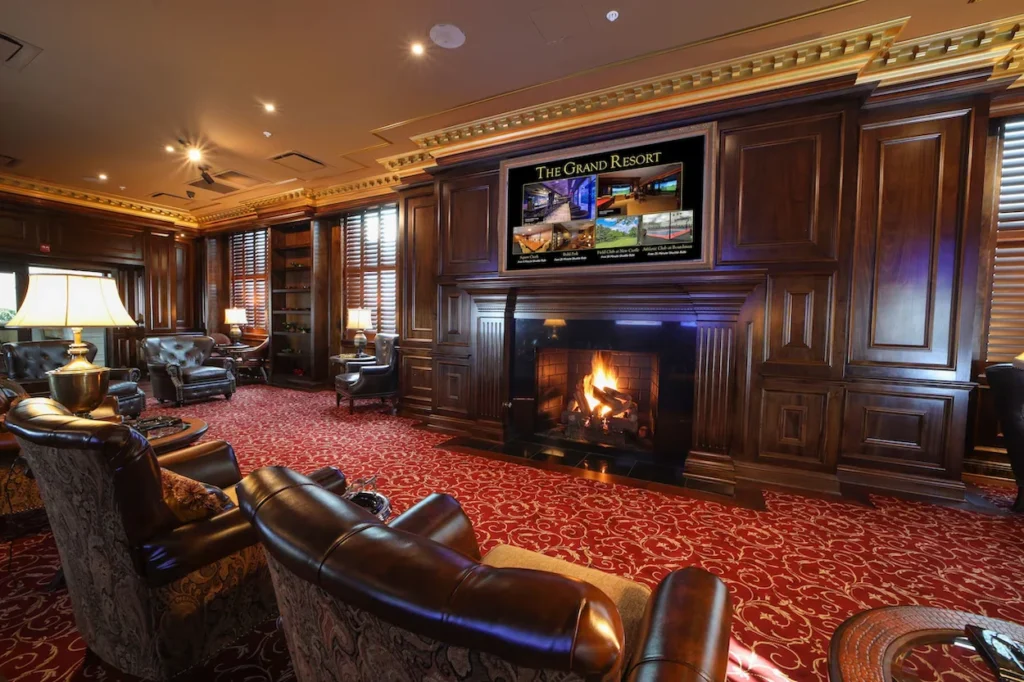 An elegant hotel lounge with dark wood walls, a fireplace, leather armchairs, and red patterned carpeting