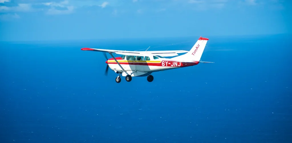 TimAir Cessna propeller plane flying low over a deep blue ocean under a clear sky