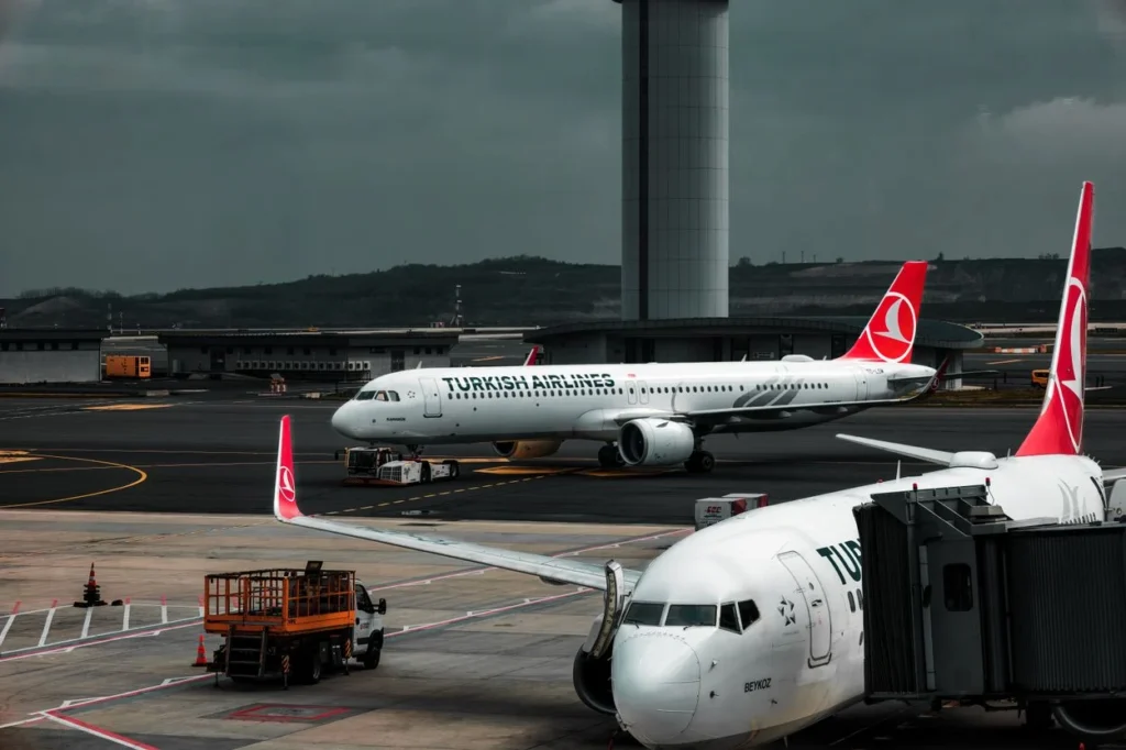 Two Turkish Airlines passenger planes parked on the tarmac near a modern control tower