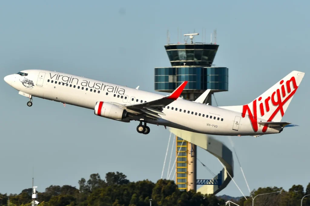 Virgin Australia Boeing 737-800 airplane taking off into the air past an airport control tower