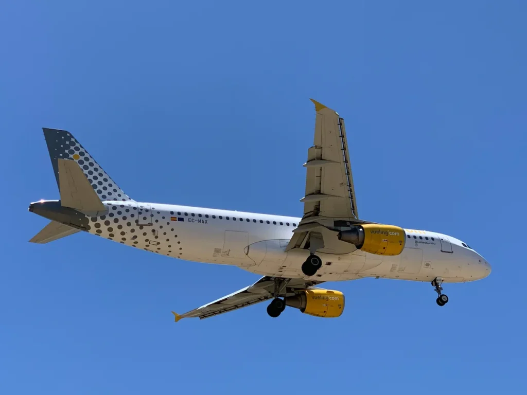 Vueling Airbus A320 commercial airplane with yellow engines flying against a clear blue sky