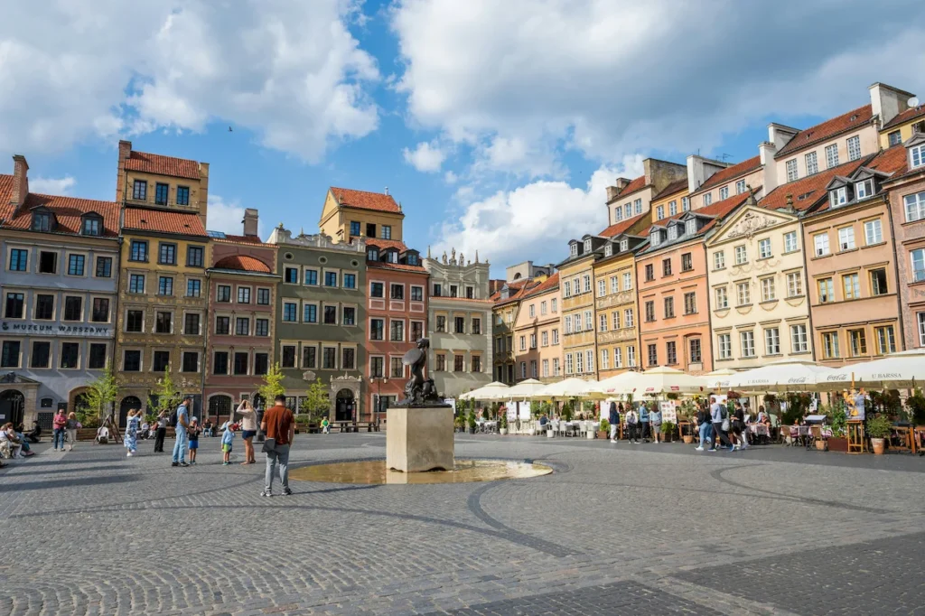 Warsaw Market Square showing colorful historic townhouses and the central mermaid monument under a blue sky